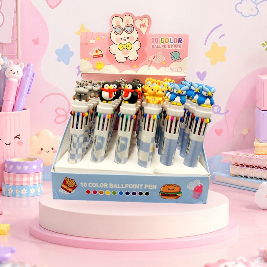 10-Colour Pen (Cute Toons): 10-colour ballpoint pens with cute toon toppers in a display box, on a pink kawaii desk — wholesale kawaii pens from Tirth Enterprise